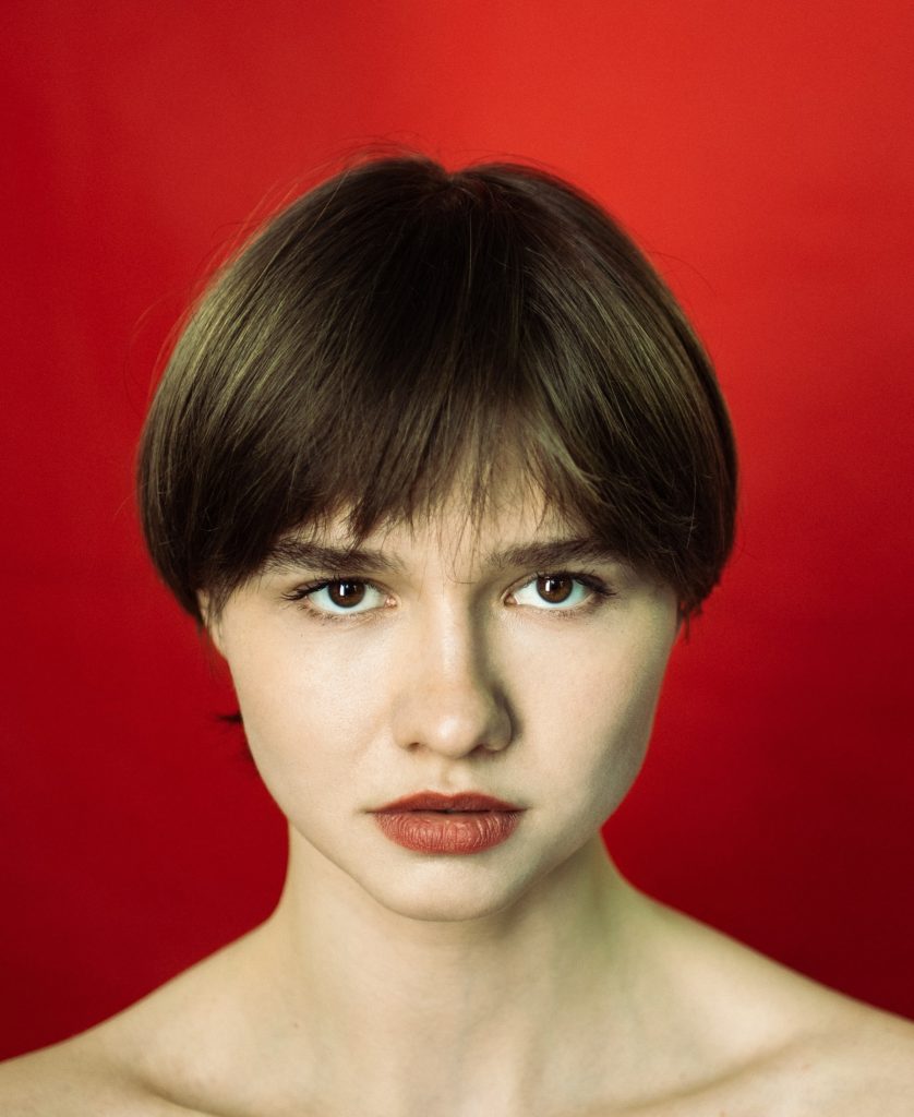 na czerwonym tle ujęcie portretowe młodej kobiety z brązowymi oczami i krótkimi ciemnymi włosami