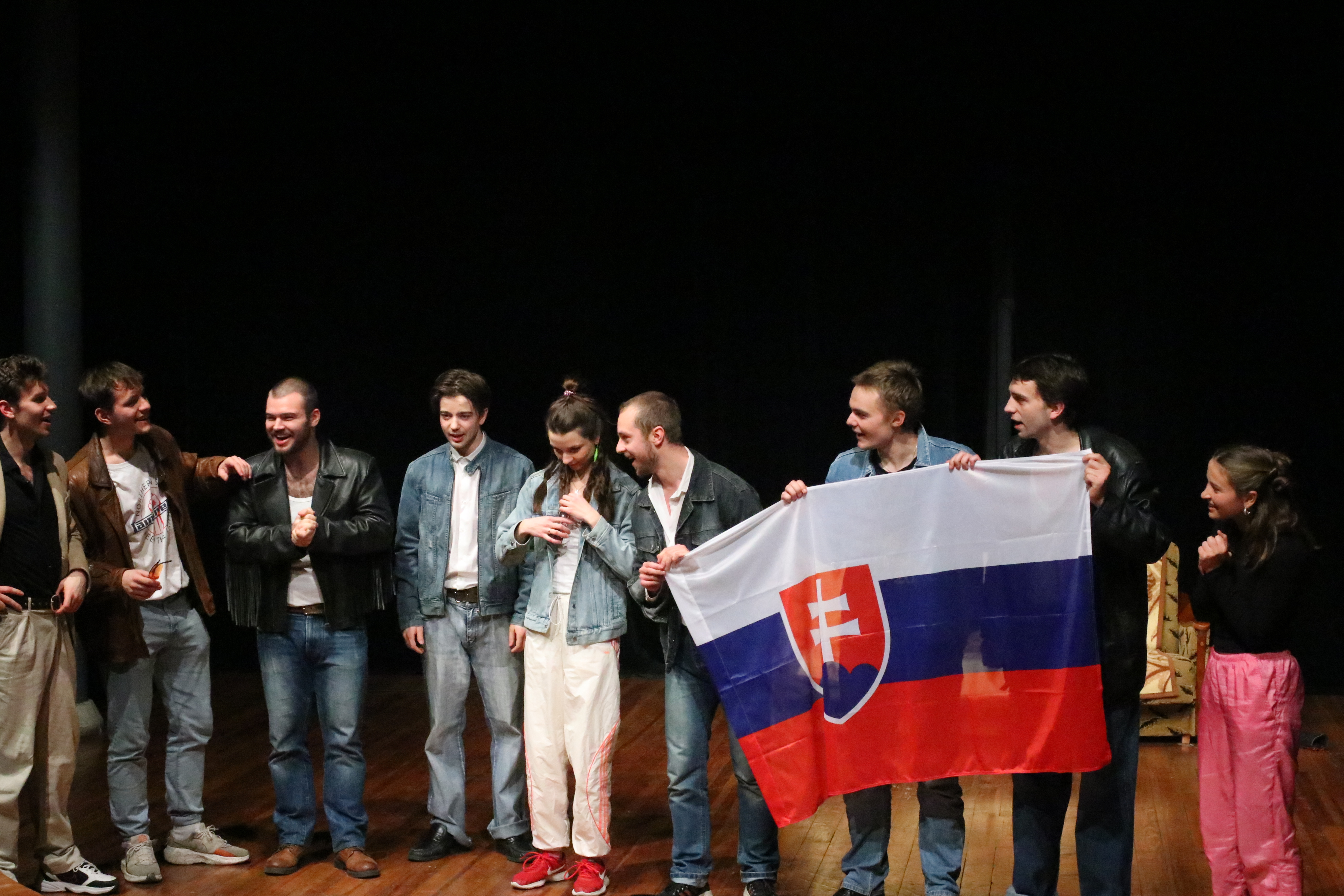 Zróżnicowana grupa osób dumnie pozująca razem, trzymając flagę Republiki Słowackiej.